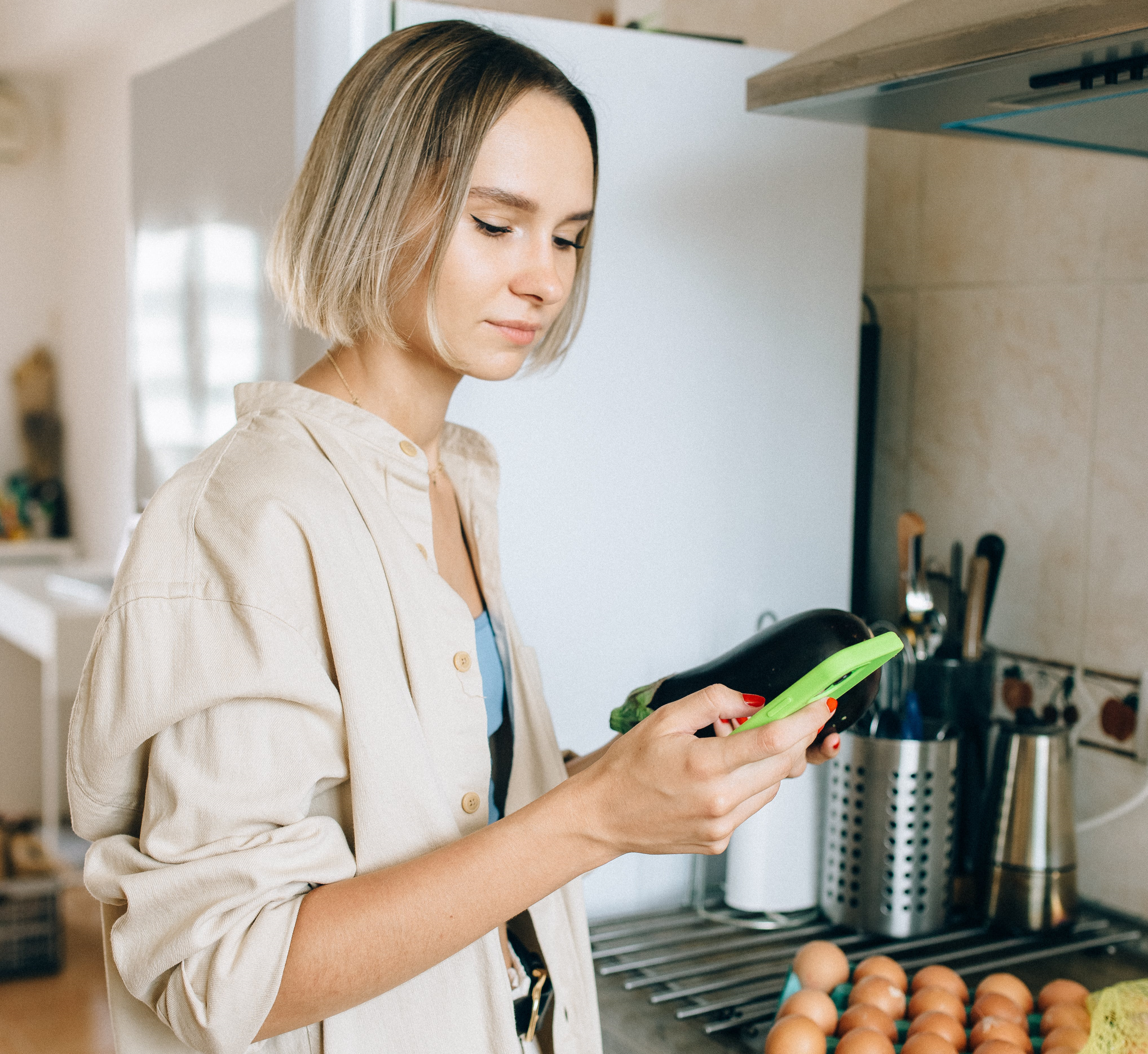Woman stands in her kitchen looking at her phone.