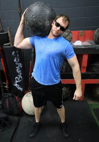 Evan holding exercise ball up on his right shoulder